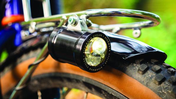 A dynamo light sits on the side of the mudguard of a bicycle wheel