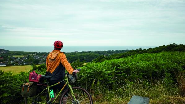 A man wearing cycling gear leaning on his bicycle overlooks a cove