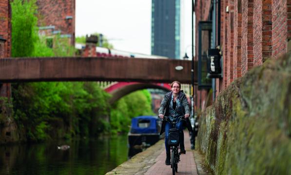 A woman cycles down a towpath along a canal in an urban setting