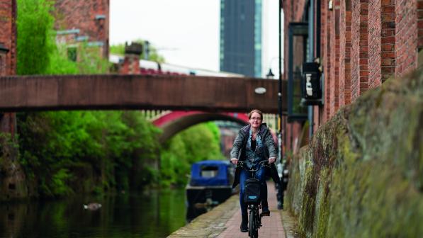 A woman cycles down a towpath along a canal in an urban setting