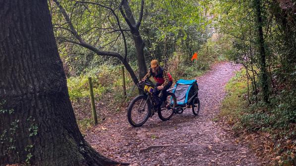 A man rides his bike with a child trailer attached to the rear on a cycle path
