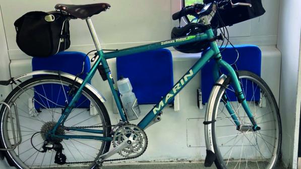 A bicycle leans against folded chairs on a train in the bicycle carriage. It's carrying rear and front rack bags