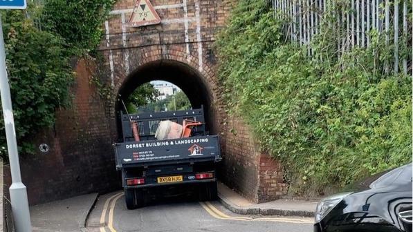 A large vehicle driving through the very narrow Keyhole Bridge underpass, nearly unable to fit through