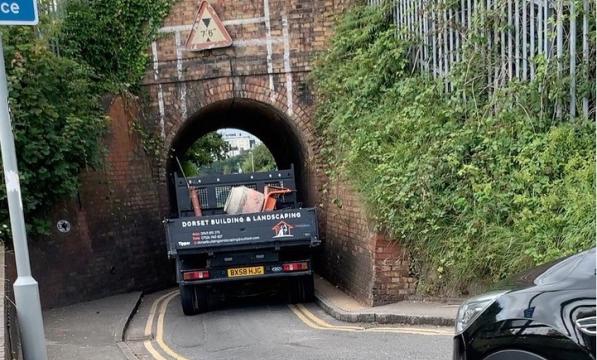 A large vehicle driving through the very narrow Keyhole Bridge underpass, nearly unable to fit through