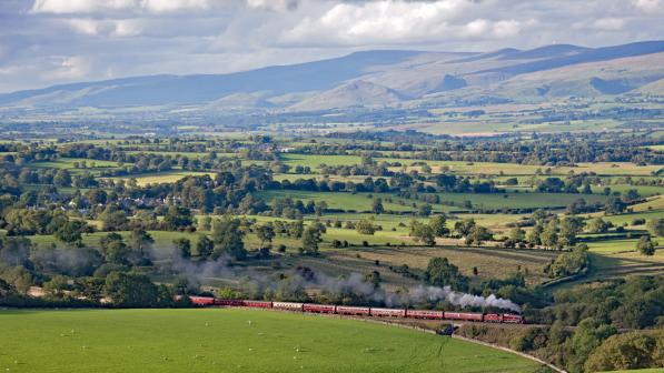 Steam train crossing a viaduct in a lush green valley