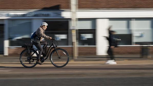 A woman wearing white helmet and purple leggings whizzes along on an e-cycle, background blurred