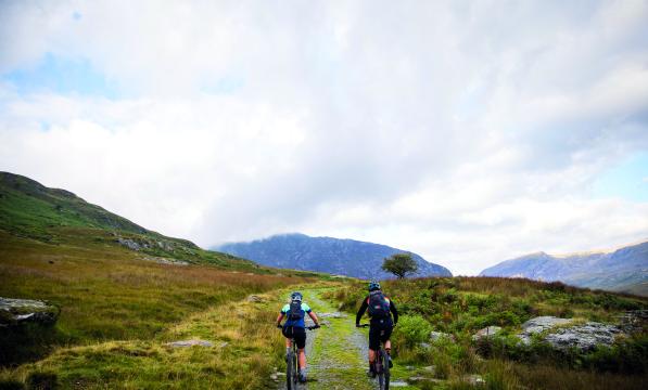 A man and a woman cycle along a rocky path along a Welsh mountain range