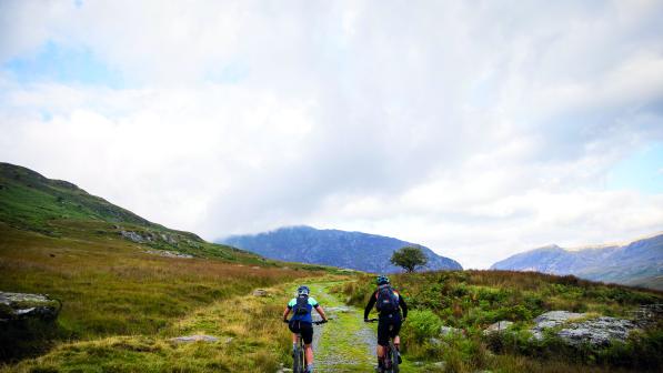 A man and a woman cycle along a rocky path along a Welsh mountain range