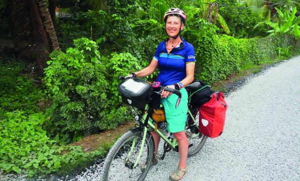 A woman stands over an adventure bicycle which is loaded with pannier bags. She is wearing a helmet and casual summer clothes