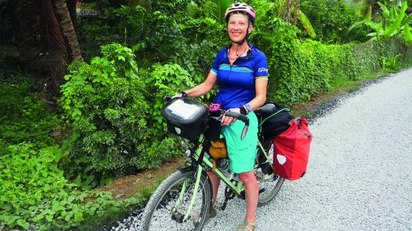 A woman stands over an adventure bicycle which is loaded with pannier bags. She is wearing a helmet and casual summer clothes