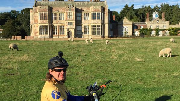 Man sitting on a handcycle in the sunshine in front of a stately home