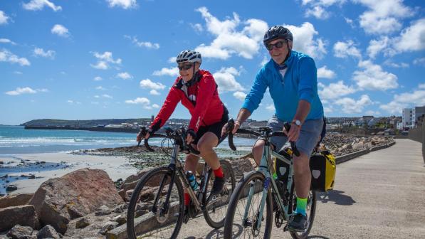 A man and woman cycle along a coastal path