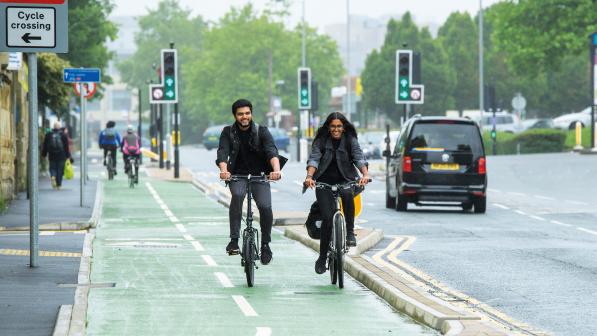 A male and female cyclist ride down a segregated cycle lane next to a busy road