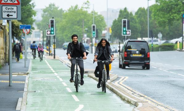 A male and female cyclist ride down a segregated cycle lane next to a busy road