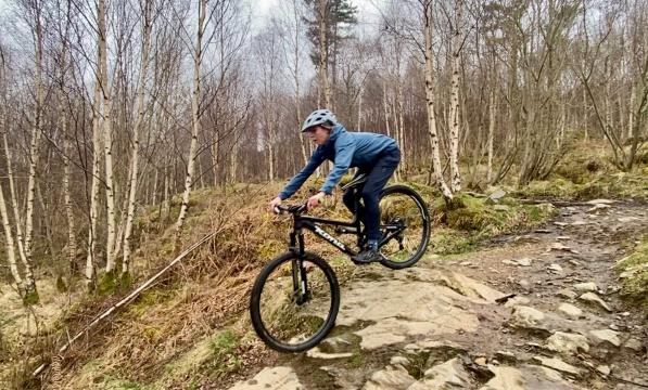 A women wearing a grey helmet, blue jacket and trousers rides a mountain bike downhill in Scotland
