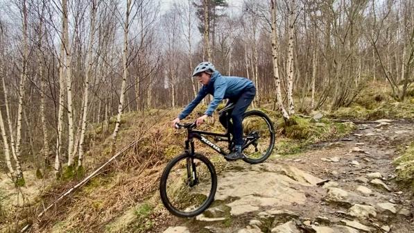 A women wearing a grey helmet, blue jacket and trousers rides a mountain bike downhill in Scotland