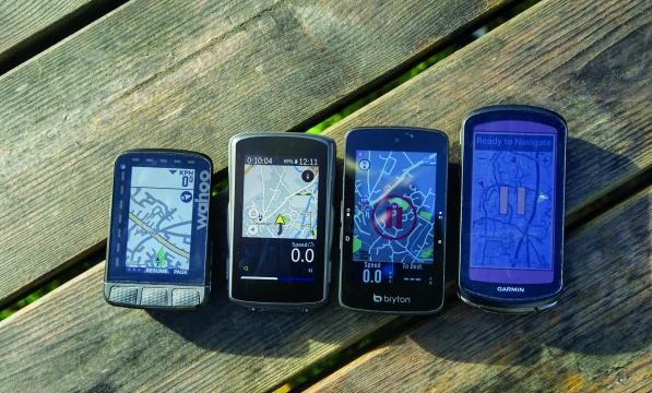 Four GPS bicycle computers are laid in order of size on a picnic bench, each of them displaying a map view.