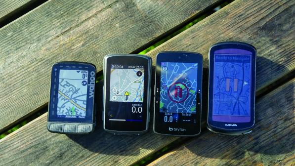 Four GPS bicycle computers are laid in order of size on a picnic bench, each of them displaying a map view.