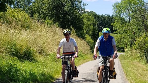 A man and a woman are cycling towards the camera on a quiet road in warm conditions