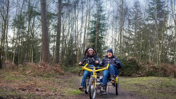 two women riding a twinbike tandem in the forest 