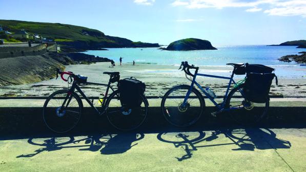 Two bicycles are propped up against a low wall in front of a beach and sea view