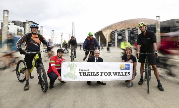 Several people with bikes stand behind a banner reading 'Support Trails for Wales'