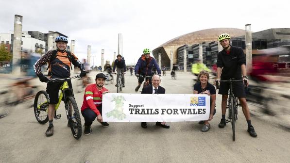 Several people with bikes stand behind a banner reading 'Support Trails for Wales'