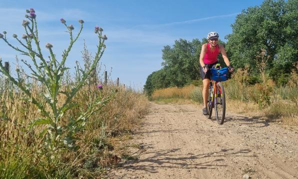 Woman cycling towards the camera on a sandy gravel track in the sunshine