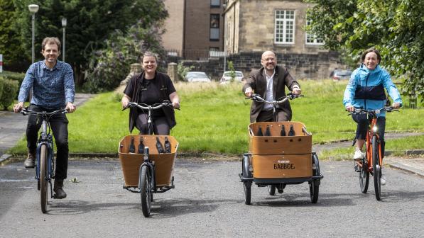 Active Travel Minister Patrick Harvie is riding a cargo bike, beside Suzanne Forup of Cycling UK who is riding a standard bike and representative from Bike for Good in Glasgow. The is a green space behind them