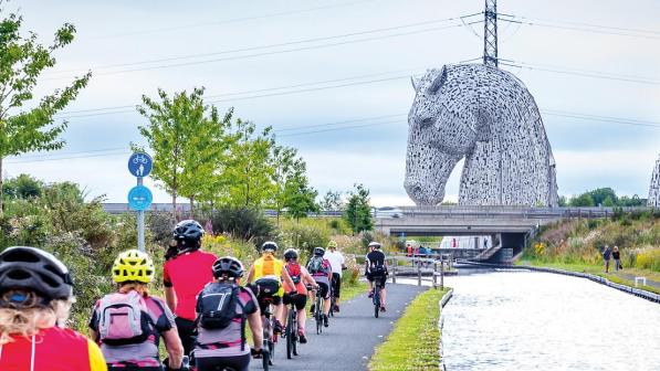 Cyclists riding along a towpath towards sculptures of horses