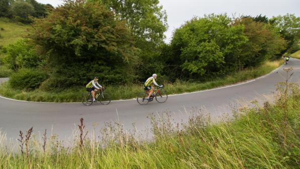 Two riders in close pursuit come out of a steep corner into a climb on a country road in the Surrey Hills