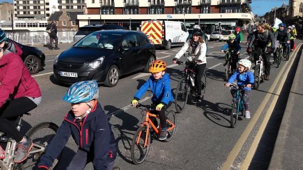 Children and adults riding across a bridge on a Kidical mass ride