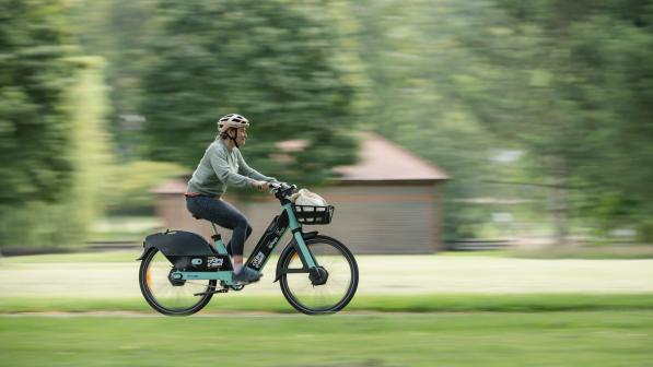 Woman whizzes through park on green TIER e-cycle on a sunny day