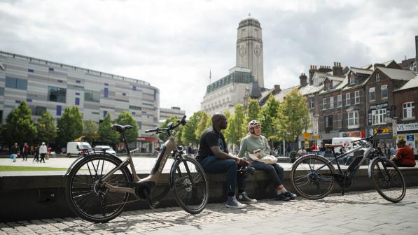 Two people sit next to their e-cycles in Luton city centre on a sunny day