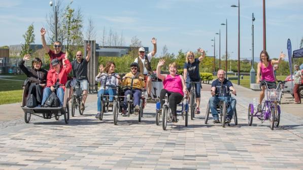A group of people riding various types of cycles all waving at the camera