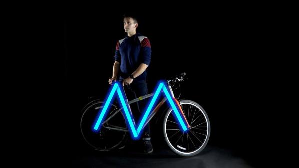 A cyclist standing behind a bike, performing an M check. 
