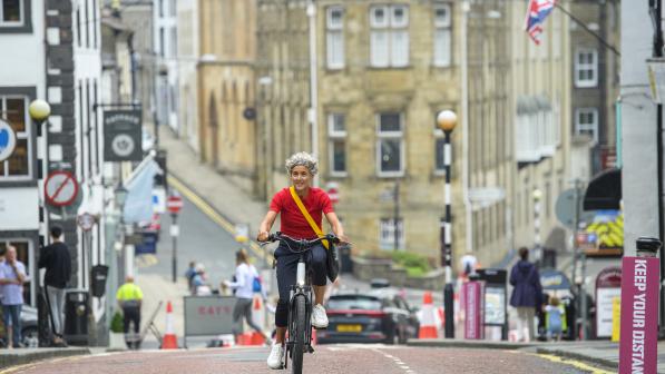 A woman wearing a red t-shirt pedals uphill on a sunny day in England