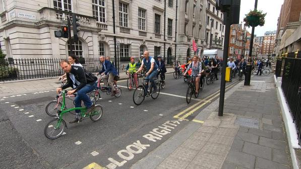 A big group of people are cycling along a London street. There is a mix of bikes and people