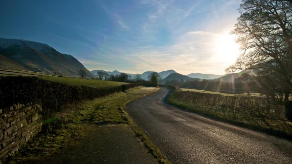 A country lane winding through fields, with mountains in the background