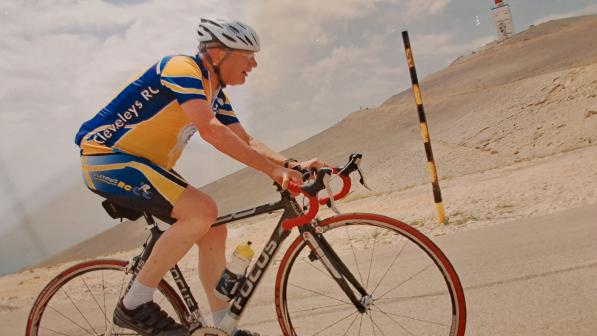 A man wearing a helmet rides a bicycle up a steep hill in a barren landscape