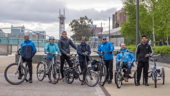 A group of people with various adaptive and standard bicycles posing outdoors in an urban setting, highlighting the inclusivity of Cycling UK's accessible cycling programs.