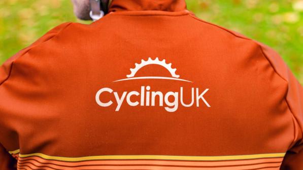 Photo of someone wearing an orange cycling jersey with the new Cycling UK logo on the back