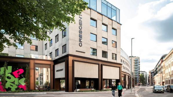 View of Crescent, a modern office building in central Bristol, with bold signage, large windows, and a tree-lined street in the foreground. Two people walk past the entrance on a bright day.