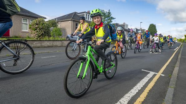 A young boy in school uniform smiles as he cycles past the camera as part of a group bike bus ride along a street