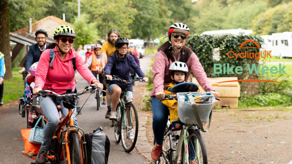 Group of cyclists on a path cycling through a park with two women at the front, one with a small child on the bike too