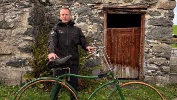 Ross standing outside holding his bike in front of a stone building