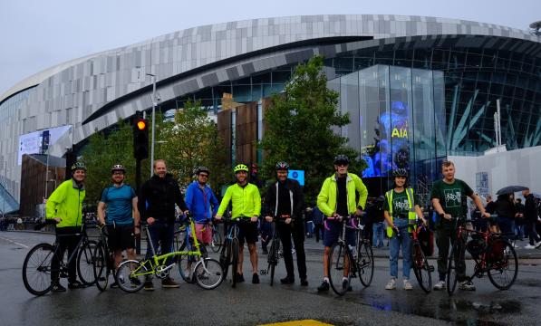 Nine attendees of led ride from Liverpool Street Station to Tottenham Hotspur Stadium, standing outside stadium with bikes.