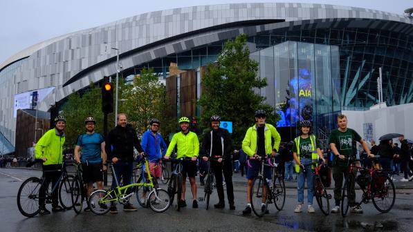 Nine attendees of led ride from Liverpool Street Station to Tottenham Hotspur Stadium, standing outside stadium with bikes.