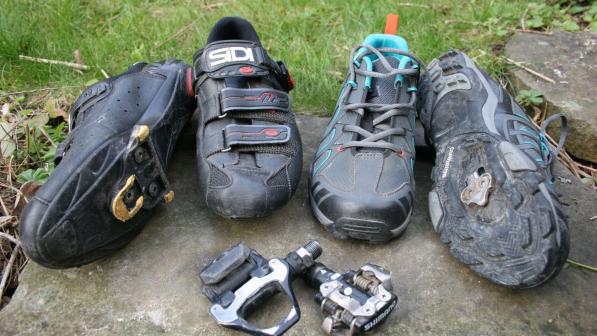 Four different types of clipless cycling shoes, with one lying on its side to show the cleat. In front are two types of clipless pedals