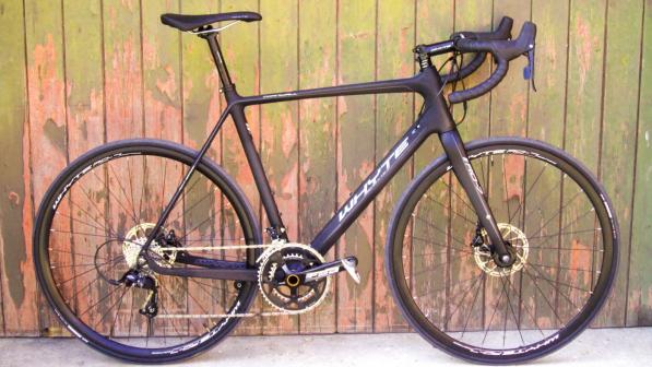 A matt purple road bike is leaning against a wooden fence